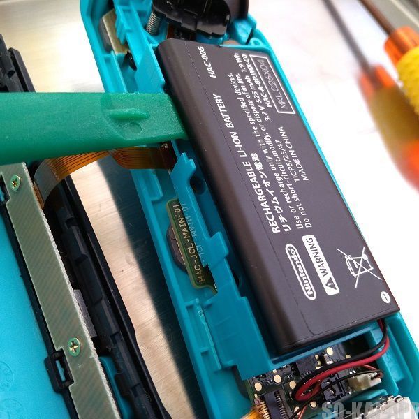 Nintendo Switch の Joy-Con(左) のバッテリーを緑の道具を使って持ち上げるところの写真